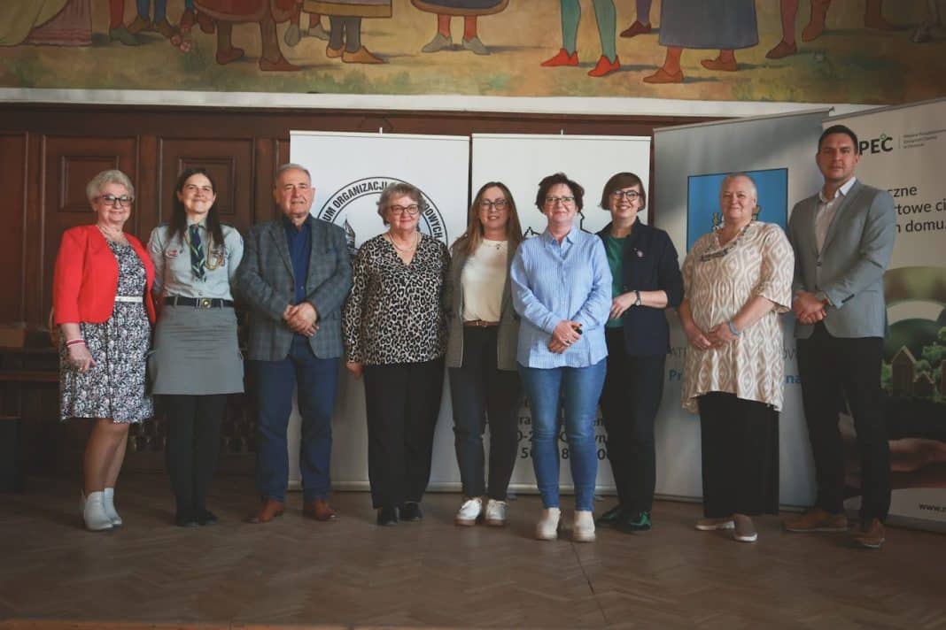 Grupa przedstawicieli organizacji społecznych na spotkaniu w Olsztynie, stojąca przed bannerami.