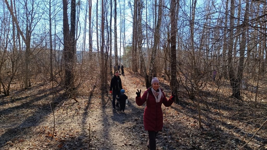 Grupa ludzi sprzątających Lasek Pieczewski w słoneczny dzień, wśr&oacute;d drzew i odpad&oacute;w.