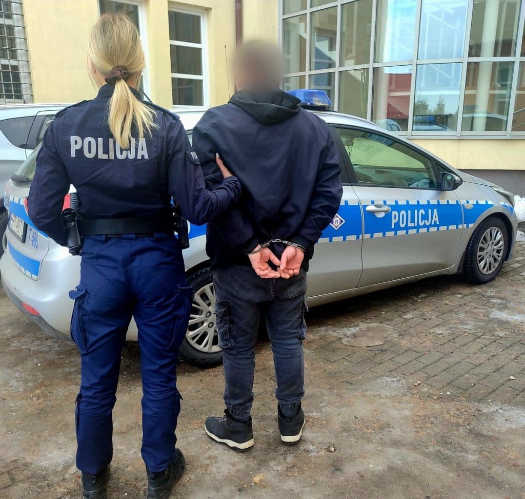 Policjantka prowadzi zatrzymanego mężczyznę do radiowozu na ulicy.