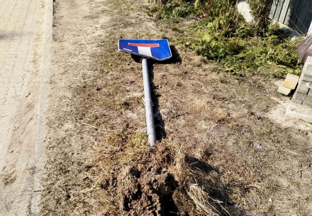 Przewr&oacute;cony znak drogowy na poboczu, obok wykopany ziemią teren.