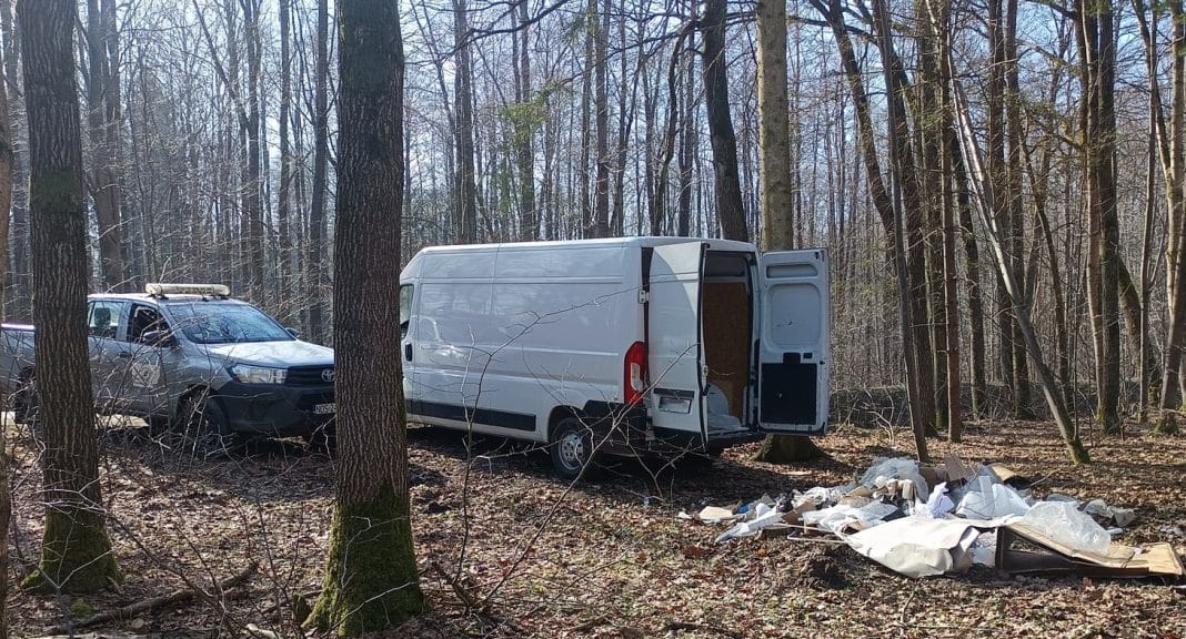 Samoch&oacute;d i samoch&oacute;d dostawczy w lesie, wok&oacute;ł porozrzucane odpady remontowe.