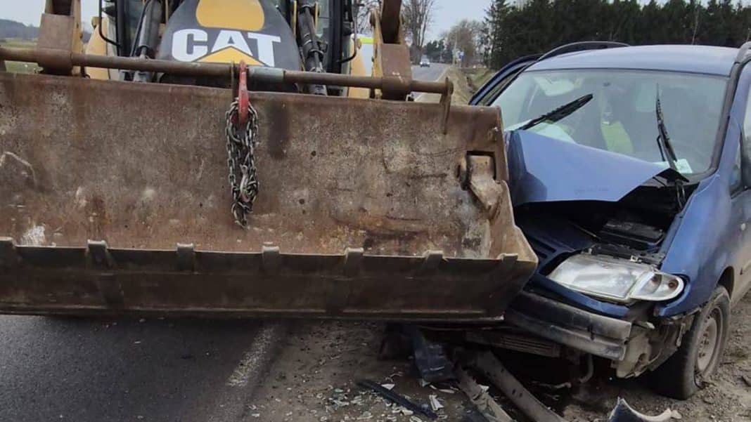 Zdjęcie przedstawia zderzenie samochodu osobowego z koparką na drodze, z widocznymi uszkodzeniami pojazd&oacute;w.