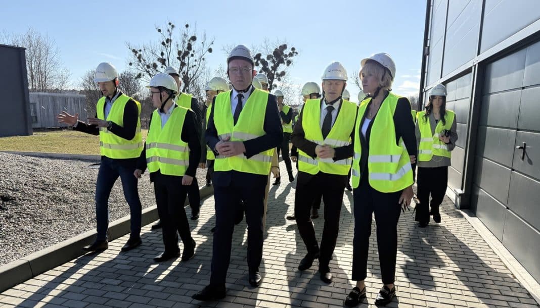 Grupa os&oacute;b w kaskach i kamizelkach odblaskowych podczas wizyty na placu budowy ciepłowni.