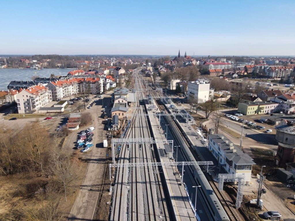 Widok na nowoczesne przejście pod peronami na stacji kolejowej w Ostr&oacute;dzie, z windami i torami w tle.