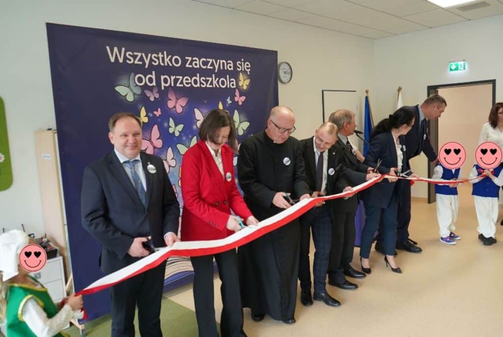 Uczestnicy oficjalnie otwierają nowoczesne przedszkole w Jonkowie, trzymając czerwoną wstęgę.