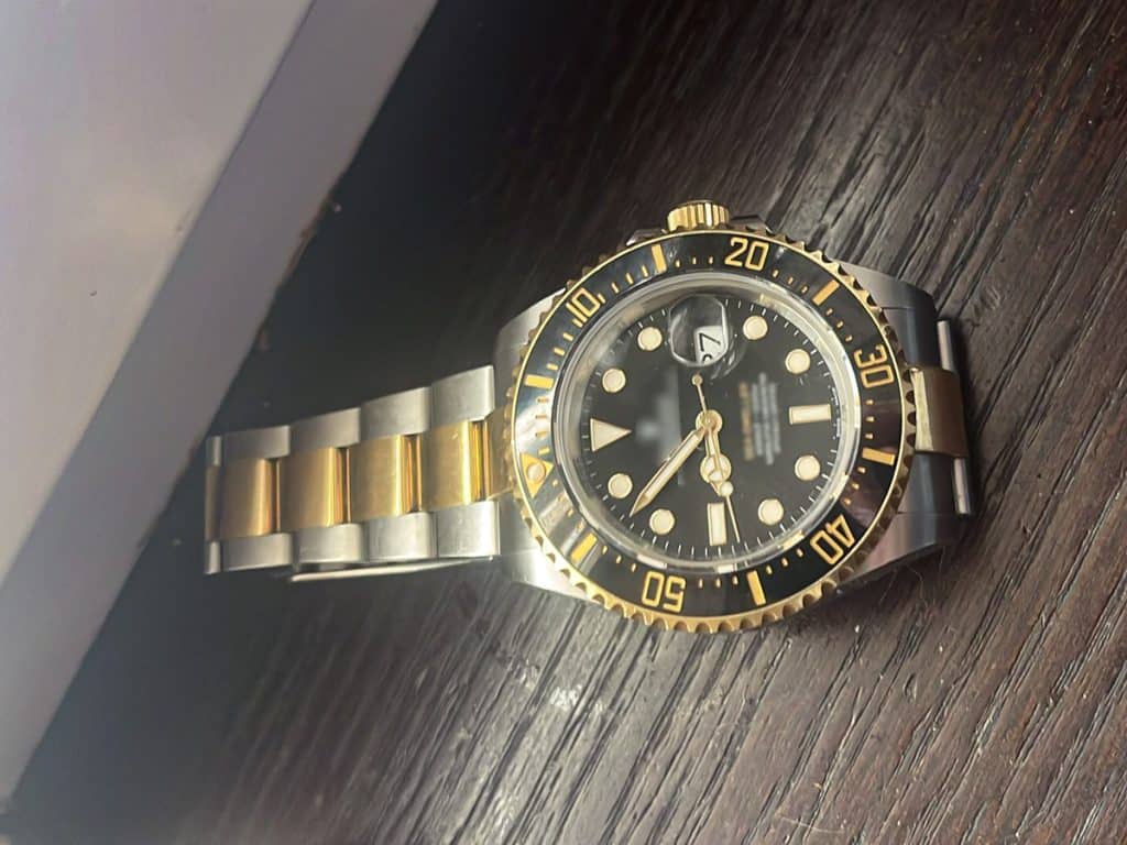 Złota i srebrna zegarek na drewnianym blacie, widoczny datownik i wskaz&oacute;wki.