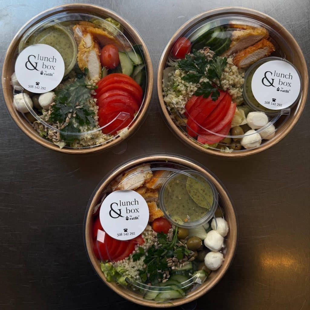 Trzy pudełka z zdrowymi lunchami, zawierającymi warzywa, sery i sosy, na ciemnym tle.