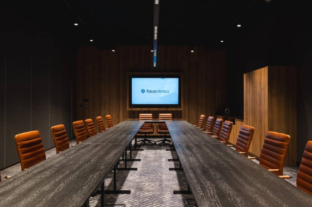 Nowoczesna sala konferencyjna w hotelu z drewnianymi panelami i dużym ekranem.