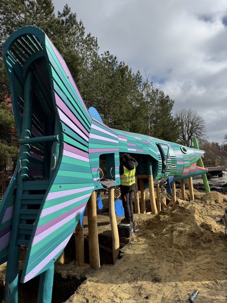 Kolorowa konstrukcja przypominająca rybę na placu budowy w Giżycku, w trakcie montażu.