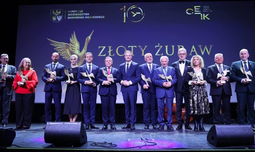 Grupa os&oacute;b na scenie podczas uroczystej gali z okazji 10-lecia lotniska w Szymanach, trzymająca statuetki.