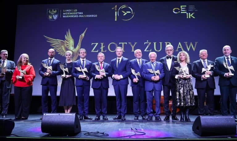 Grupa os&oacute;b na scenie podczas uroczystej gali z okazji 10-lecia lotniska w Szymanach, trzymająca statuetki.