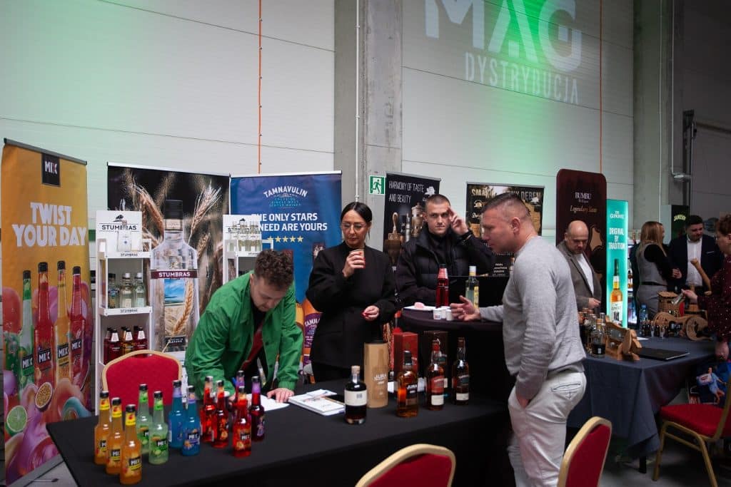 Stoisko z r&oacute;żnorodnymi alkoholami i napojami na targach w Gdańsku, z uczestnikami rozmawiającymi i degustującymi.