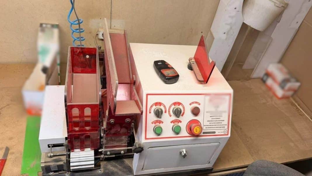 Urządzenie do produkcji papieros&oacute;w i zabezpieczone wyroby tytoniowe na stole.