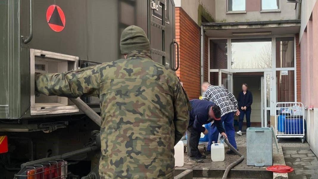 Wojsko i służby ratunkowe dostarczają wodę mieszkańcom w Olecku, w tle budynek mieszkalny.