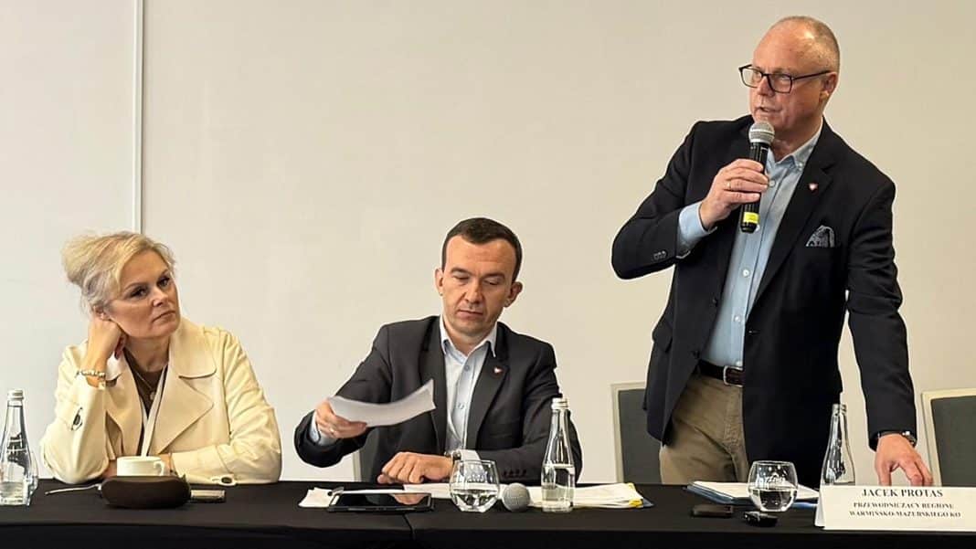 Politycy KO podczas posiedzenia w hotelu w Olsztynie, siedzą przy stole z dokumentami i mikrofonem.