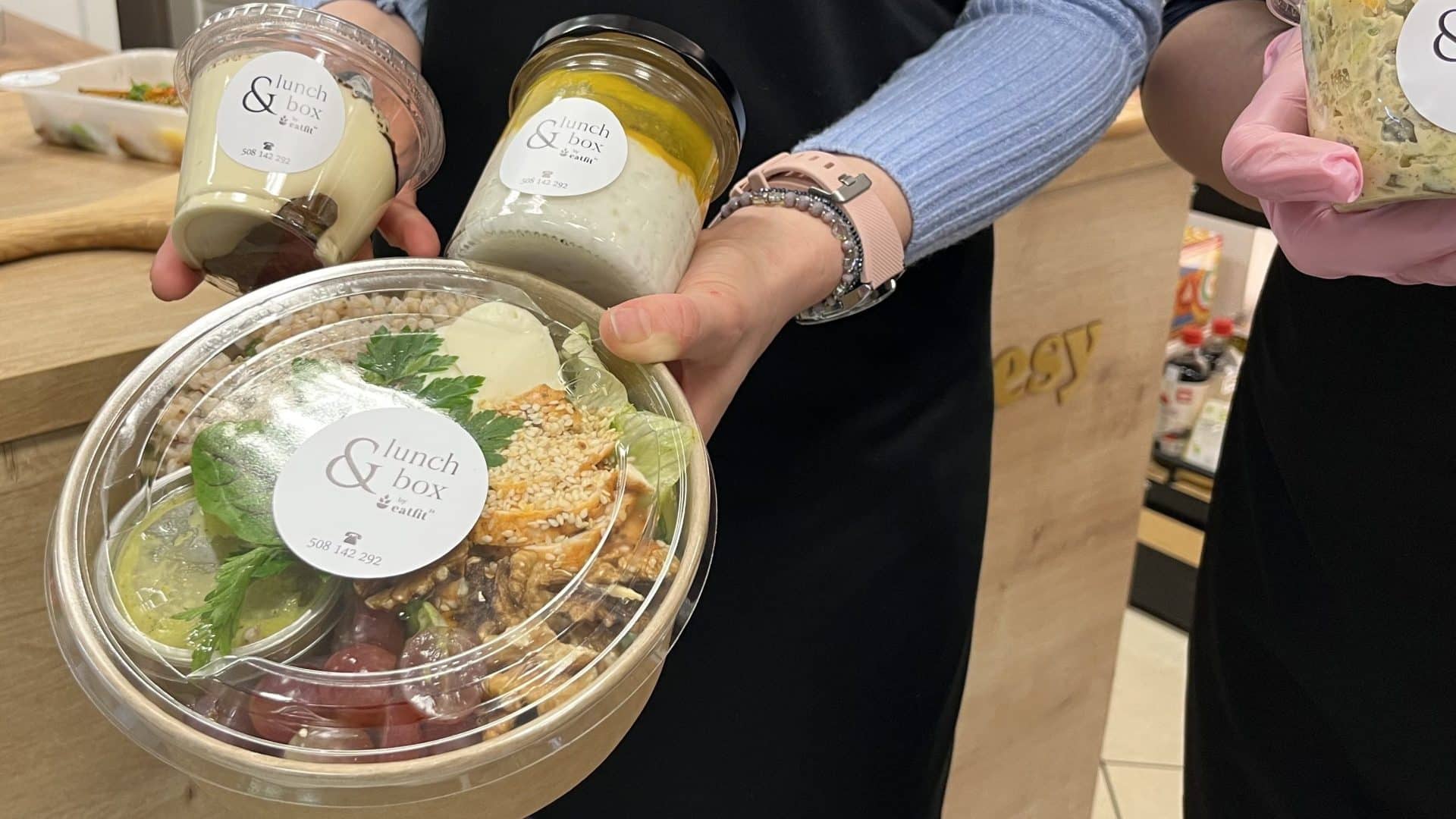 Osoba trzymająca zestaw zdrowych lunch&oacute;w i sałatek w opakowaniach na wynos.