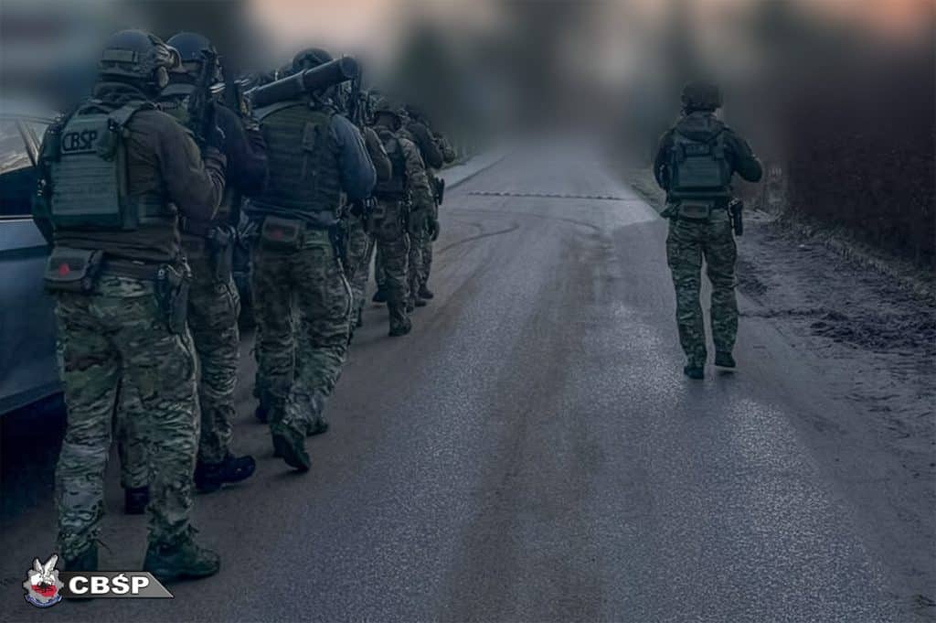 Grupa funkcjonariuszy CBŚP podczas akcji na drodze, w tle mgła i rozświetlone niebo.