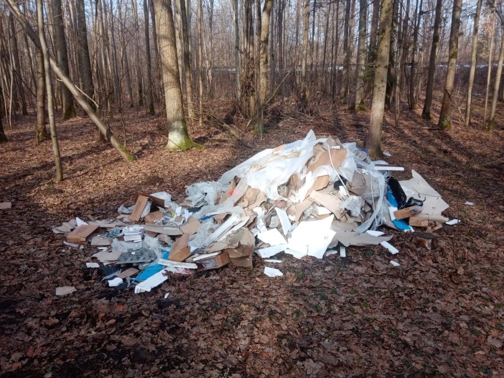 Wyrzucone odpady remontowe w lesie, papier i plastiki na ziemi wśr&oacute;d drzew.