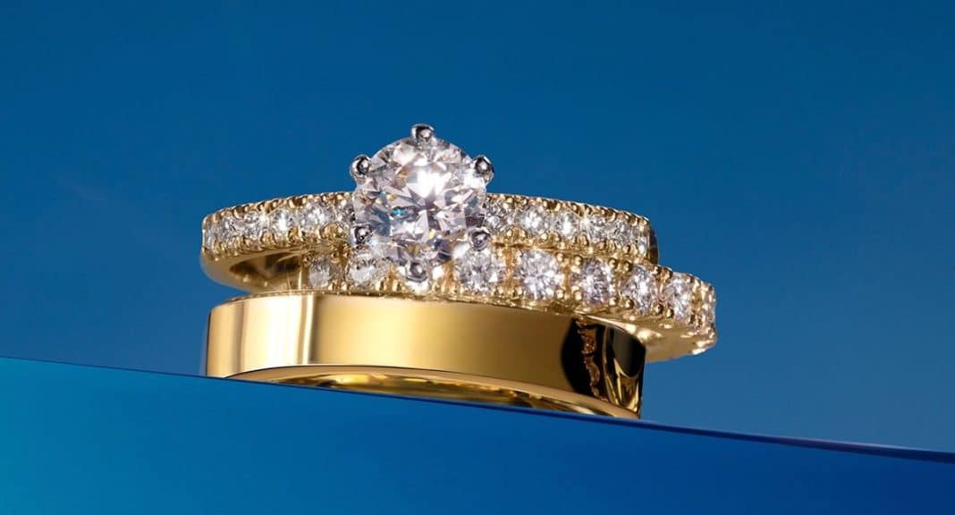 Zestaw biżuterii składający się z pierścionka zaręczynowego i obrączek na niebieskim tle.