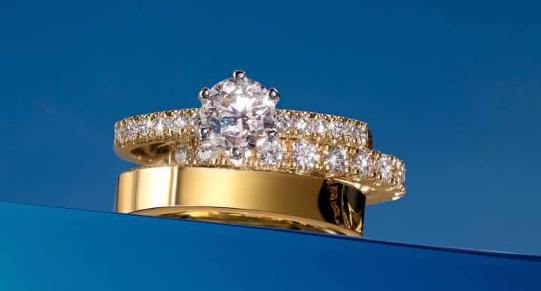 Zestaw biżuterii składający się z pierścionka zaręczynowego i obrączek na niebieskim tle.