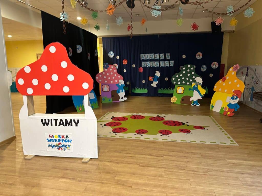 Przestrzeń przedszkolna z kolorowymi dekoracjami i sceną do występ&oacute;w dzieci.