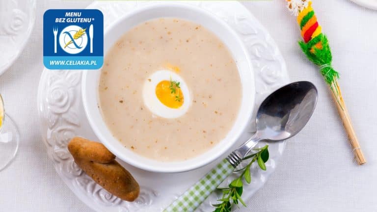 Zupa w białej misce z jajkiem na twardo, obok łyżka i chlebek, na świątecznym stole.