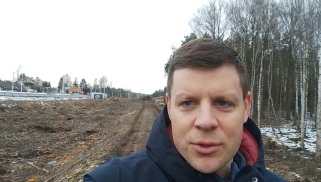 Mężczyzna na tle budowy drogi w lesie, w tle drzewa i fragmenty śniegu.