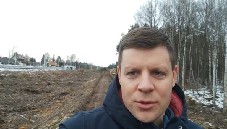 Mężczyzna na tle budowy drogi w lesie, w tle drzewa i fragmenty śniegu.