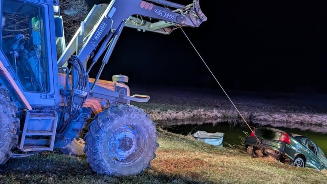 Samoch&oacute;d osobowy w wodzie, wyciągany przez ciężki sprzęt ratowniczy w nocy.
