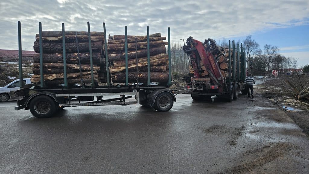 Samoch&oacute;d przewozi płyty z drewna na tle nieba i okolicznych drzew, w trakcie budowy drogi w Olsztynie.
