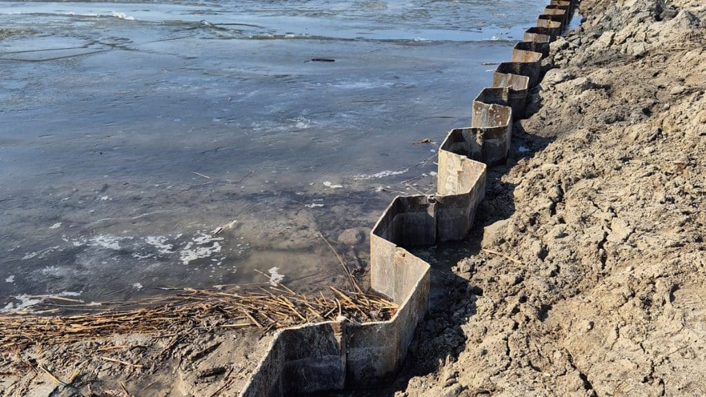 Zbliżenie na brzeg kanału na Mazurach z widocznymi metalowymi elementami zabezpieczającymi brzeg.