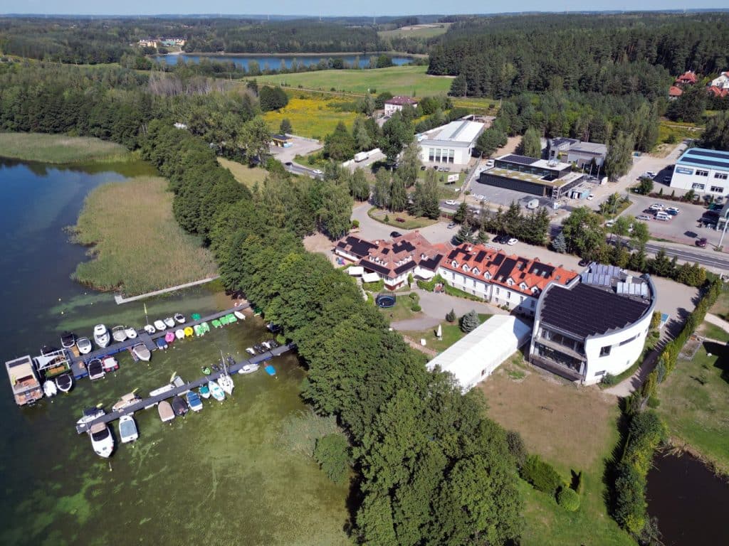 Widok na jezioro Ukiel w Olsztynie z drona, otoczone zabudową i zielenią, z widocznymi łodziami i brzegami.