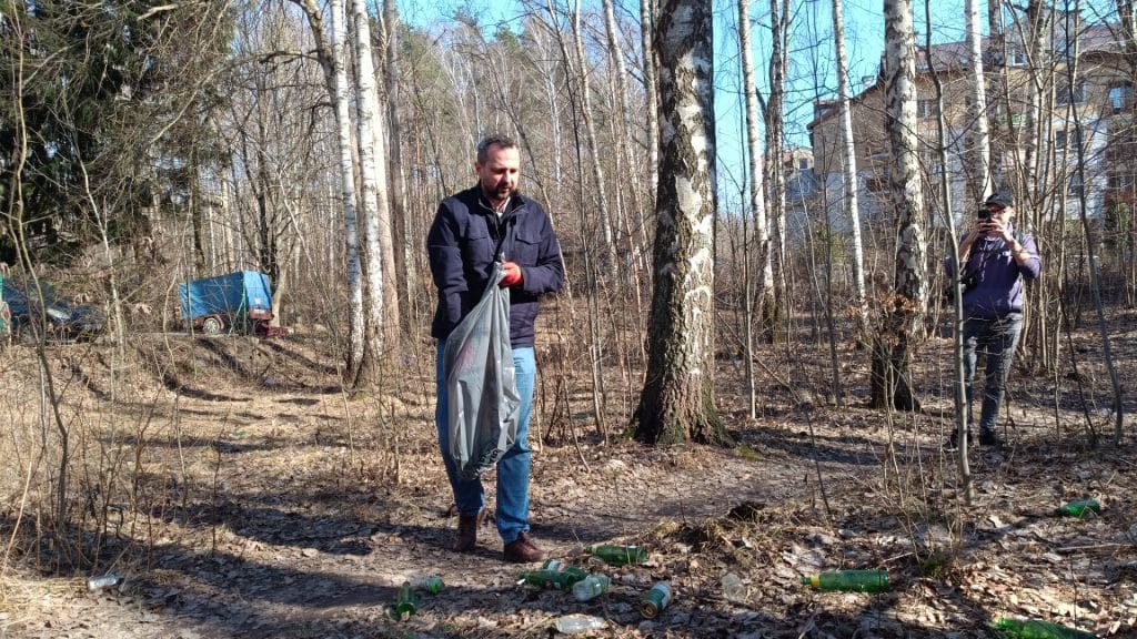 Mężczyzna sprzątający las w Olsztynie, wok&oacute;ł porozrzucane butelki i odpady.