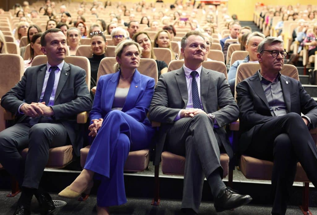 Grupa dorosłych siedzi na widowni podczas wydarzenia w dużej sali konferencyjnej.