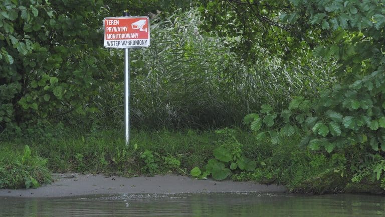 Zbliżenie na brzeg jeziora Ukiel z zakwitami i glonami, widoczny zakaz wstępu na teren prywatny.