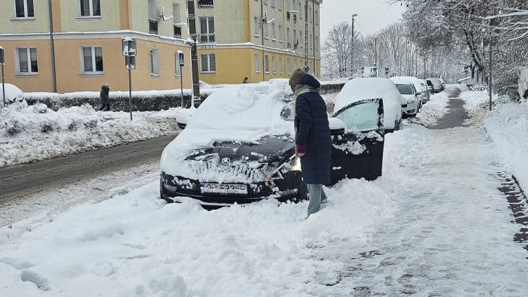 Osoba odśnieżająca samoch&oacute;d na zaśnieżonej ulicy w Olsztynie.