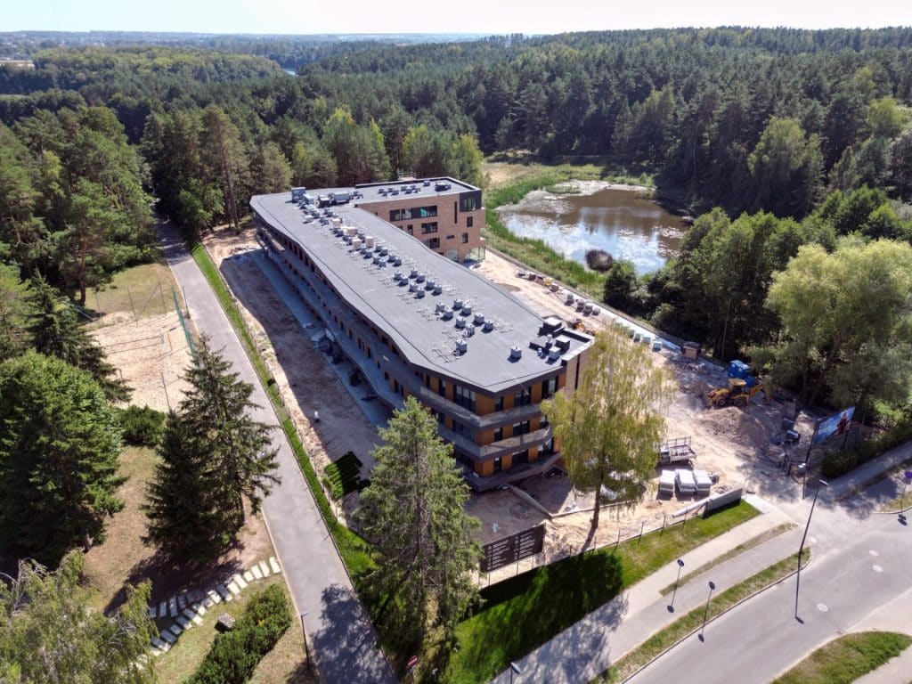 Nowoczesny budynek w otoczeniu las&oacute;w i jeziora Ukiel, trwają prace budowlane.
