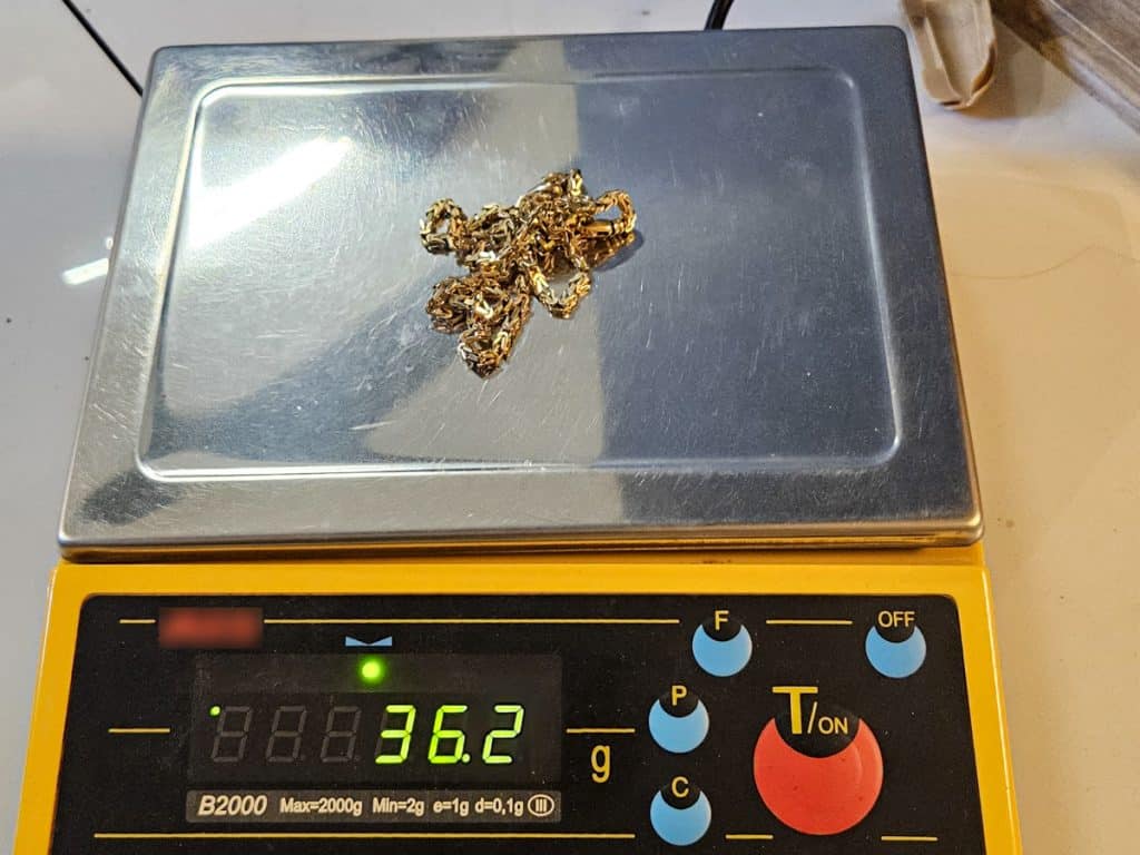 Złoty łańcuch na wadze, wskazujący 36,2 grama, na stole w pomieszczeniu.