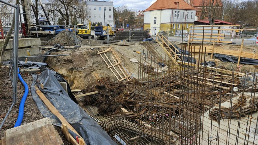 Budowa nowego obiektu usługowego w centrum Olsztyna, widoczne prace ziemne i zbrojenia.