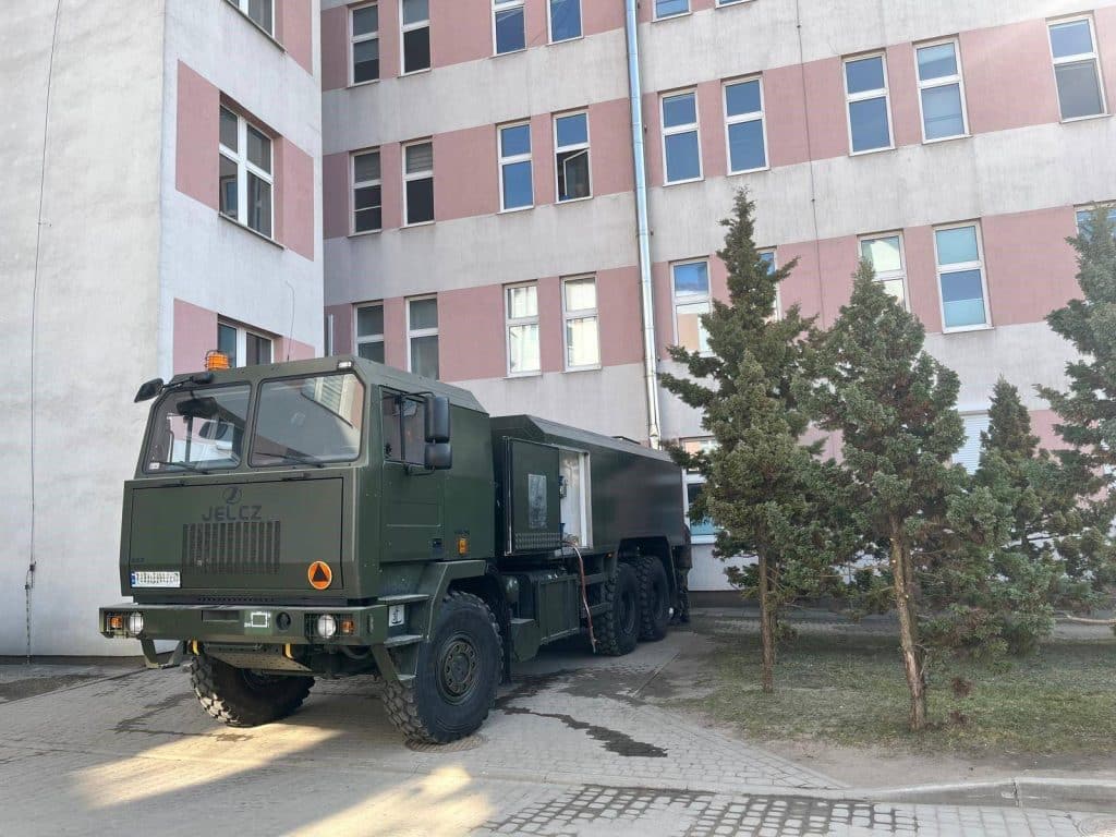 Wojsko dostarcza wodę pitną w regionie po skażeniu wody, pojazd wojskowy na tle blok&oacute;w mieszkalnych.