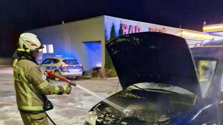 Strażak gasi pożar samochodu na stacji paliw przy DK16 w nocy.