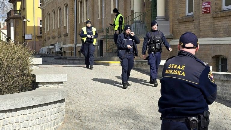 Grupa policjant&oacute;w i strażnik&oacute;w miejskich na ewakuacji urzędu w Ostr&oacute;dzie, w tle budynek magistratu.