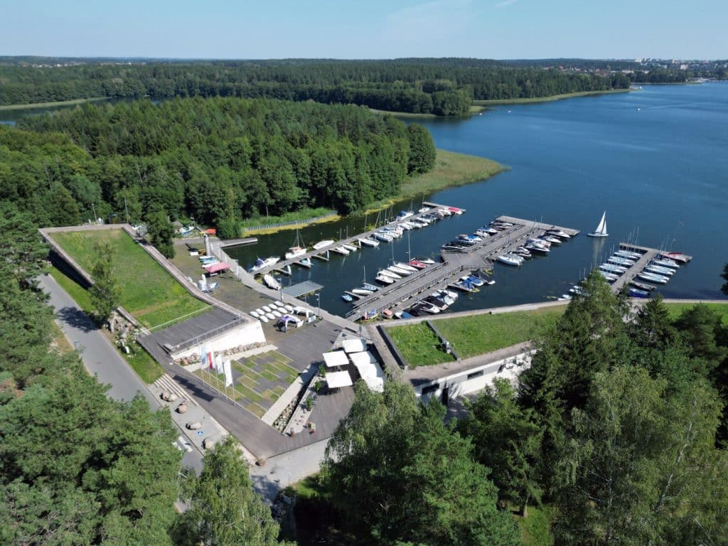 Widok na port jachtowy nad jeziorem Ukiel otoczony zielenią i zabudową brzegową.