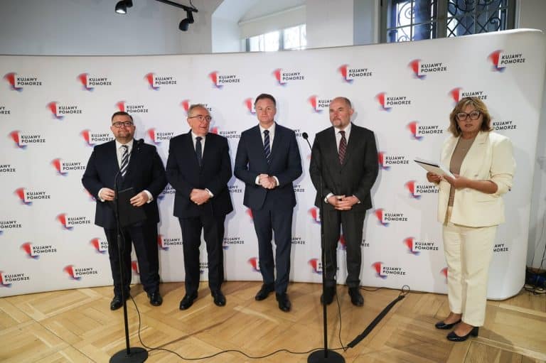 Grupa polityk&oacute;w podczas konferencji prasowej z logo Kujawy Pomorze w tle.