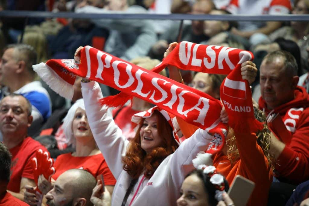 Kibice w czerwonych strojach i z szalikami wspierają reprezentację Polski podczas meczu.