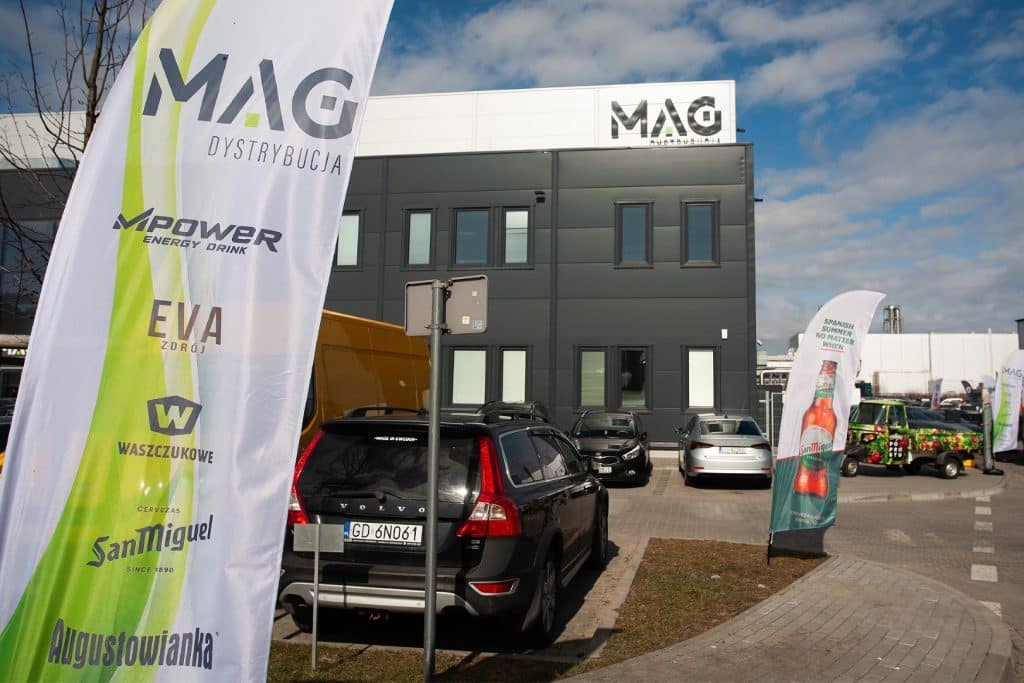 Targi biznesowe w Gdańsku z flagami i samochodami przed nowoczesnym budynkiem.