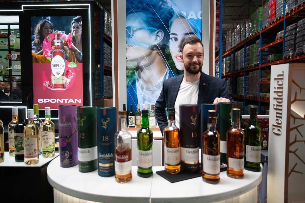 Mężczyzna prezentuje produkty alkoholowe na stoisku targowym w hali magazynowej.