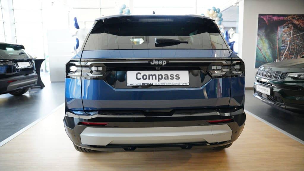 Nowy Jeep Compass w salonie samochodowym, widok z tyłu, w kolorze niebieskim i czarnym.