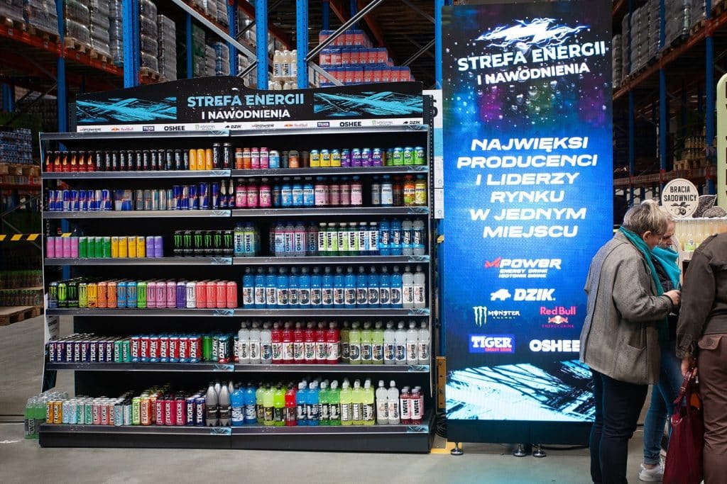 Stoisko z napojami energetycznymi i suplementami na targach w Gdańsku, w tle ekran z informacją o branży.