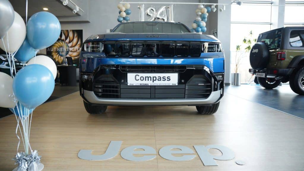 Nowy Jeep Compass na wystawie w salonie samochodowym, widoczny z przodu, w otoczeniu balon&oacute;w i innych modeli.